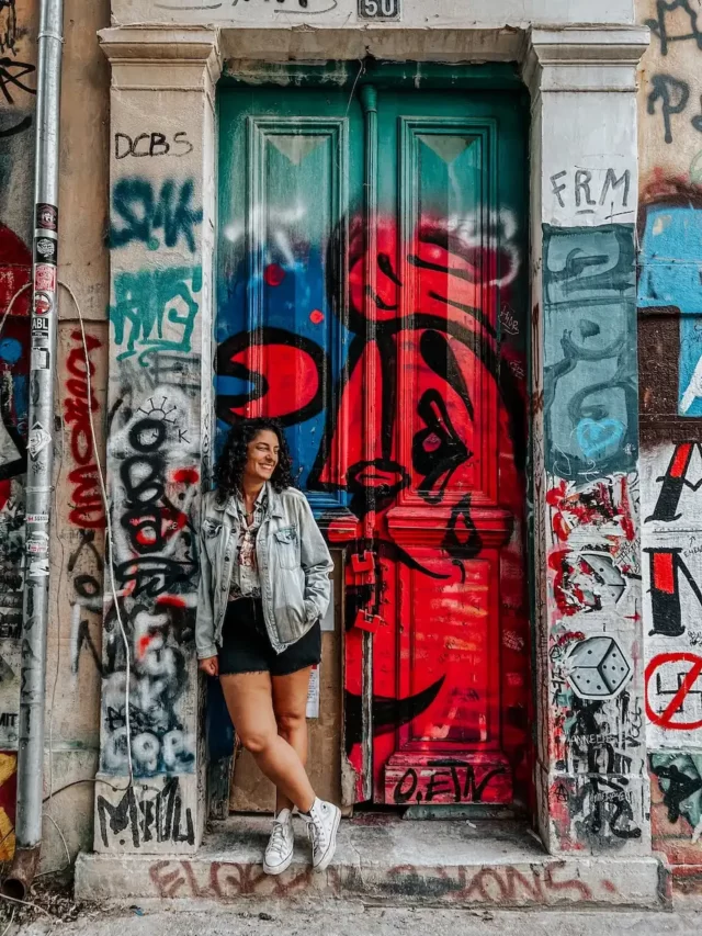 Autora em frente a porta antiga com graffitis e pixos coloridos no bairro Exarcheia, em Atenas