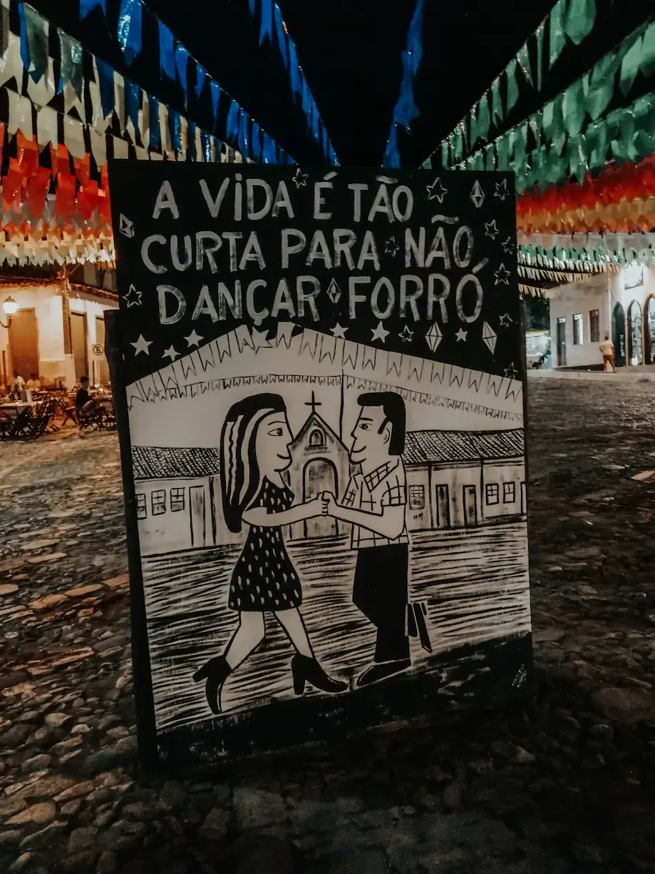 Placa escrito "A vida é muito curta para não dançar forró", com ilustração de um casal dançando na Praça de Lençóis, São João de 2019